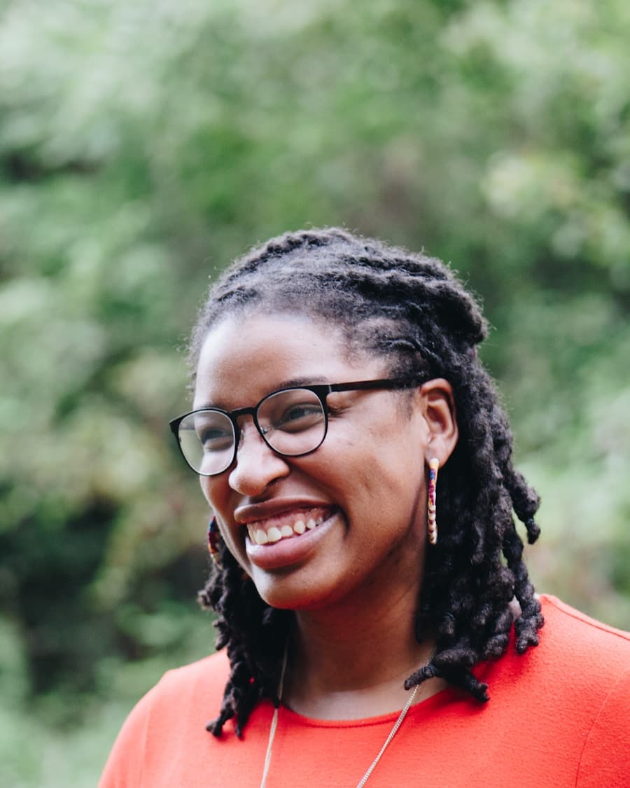 Black woman with locs smiling outdoors, ready for coaching conversation